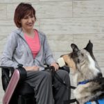 Woman in wheelchair and service dog holding a dumbbell