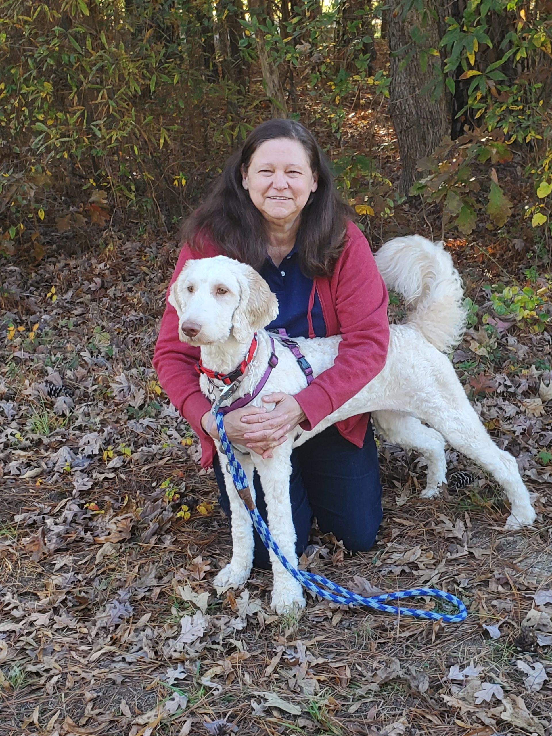 Dog trainer smiling and kneeling with her arms around a dog that is standing in front of her.