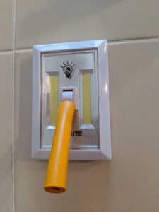 Battery operated light switch on a wall, foam tubing is on the toggle extending the length by a couple of inches.