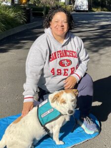 Angela Gardner sitting with her service dog a mixed bred dog in front her.