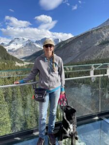 Woman standing next to dog with mountains and lake behindher